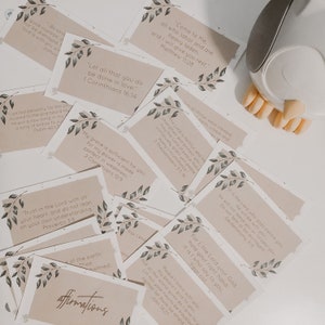 May include: A set of beige affirmation cards with green floral accents. Each card features a different Bible verse. The cards are arranged in a random order.