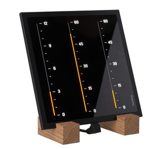 Könnte beinhalten: Eine schwarze Digitaluhr mit drei orangefarbenen LED-Balken, die die Zeit anzeigen. Die Uhr steht auf einem Holzständer und hat ein schwarzes Stromkabel.