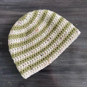 Puede incluir: Un gorro de punto de crochet a rayas verdes y blancas. El gorro está hecho con un hilo texturizado y tiene un ajuste holgado.