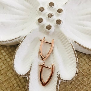 May include: A pair of rose gold hoop earrings with a v-shaped design. The earrings are on a white flower-shaped dish.