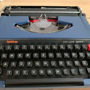 Puede incluir: Una m&aacute;quina de escribir Brother Deluxe 240T azul con un teclado negro y una tecla de tabulaci&oacute;n roja.