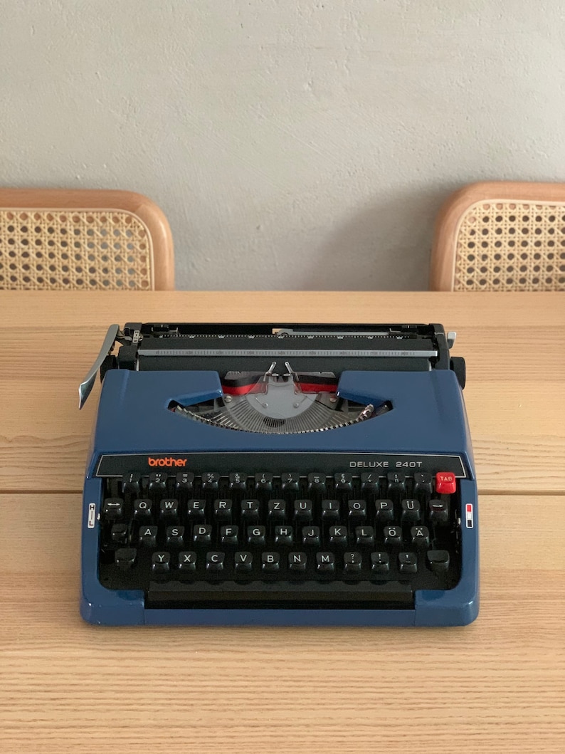 Puede incluir: Una m&aacute;quina de escribir Brother Deluxe 240T azul con un teclado negro y una tecla de tabulaci&oacute;n roja. La m&aacute;quina de escribir tiene una palanca de retorno de carro plateada y una palanca de liberaci&oacute;n de papel plateada.