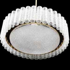 Op de afbeelding: Een ronde, witte, matte glazen plafondlamp met een gouden metalen frame. De lamp is gemaakt van veel kleine, matte glazen buizen.