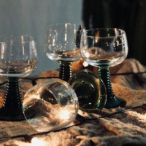 Peut inclure: Quatre verres à vin en verre transparent avec des tiges en spirale vertes sur une surface texturée brune avec des guirlandes lumineuses blanches.
