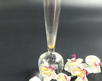 May include: A clear glass vase with a round, textured base and a tall, slender neck. The vase is decorated with small air bubbles throughout. White orchids with pink accents are arranged around the base of the vase.