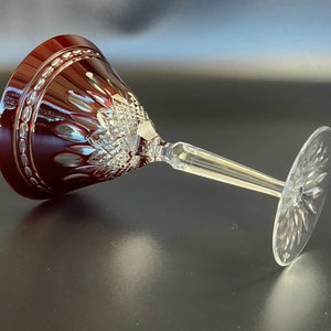 Könnte beinhalten: Ein rotes Kristall Weinglas mit einem klaren Stiel und Fuß. Das Glas hat ein geschnittenes Design und ist mit einem Diamantenmuster verziert.