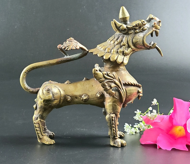 Puede incluir: Una escultura de metal dorado de una criatura m&iacute;tica con alas y una cola larga. La criatura tiene una expresi&oacute;n feroz y est&aacute; de pie sobre sus cuatro patas.