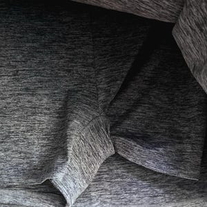 May include: Close-up of a gray athletic skort. The fabric has a textured, heathered appearance. The shorts portion is visible beneath the skirt, with seams and edges clearly defined. The garment appears to be made of a lightweight, breathable material.