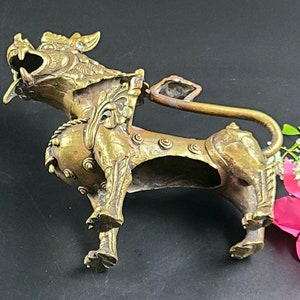 Puede incluir: Una escultura de metal dorado de un le&oacute;n m&iacute;tico con detalles intrincados. El le&oacute;n est&aacute; de pie sobre sus cuatro patas con la cabeza girada hacia un lado y la boca abierta. La escultura mide aproximadamente 15 cm de alto.