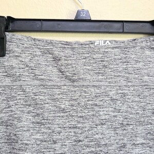 May include: Gray athletic skirt hanging on a black hanger. The skirt has a heathered pattern and the brand name "FILA" is visible. The skirt is made of a stretchy material, suitable for sports and exercise.