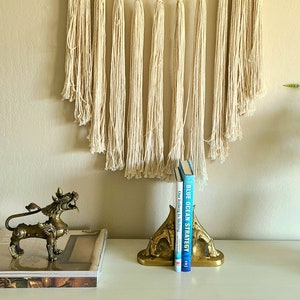 Puede incluir: Un par de sujetalibros de metal dorado con forma de criatura m&iacute;tica con un libro titulado "Blue Ocean Strategy" y otro libro titulado "Our Iceberg is Melting" entre ellos. Los sujetalibros est&aacute;n sobre una superficie blanca frente a una pared con una pared de macram&eacute;.