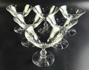 Op de afbeelding: Set van zes heldere glazen champagnecoupes met een delicaat geëtst stervormig patroon. De coupes hebben een klassieke vorm en zijn perfect om champagne of andere mousserende dranken te serveren.