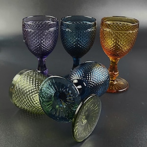 May include: Set of six colorful glass wine glasses with a diamond pattern. The glasses are in shades of purple, blue, green, and orange.