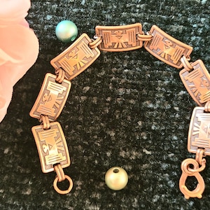 May include: A copper bracelet with a repeating pattern of stylized birds. The bracelet has a lobster clasp closure.