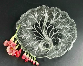 Puede incluir: Un plato de servir de vidrio transparente con un diseño intrincado en relieve que se asemeja a una rama frondosa. El plato tiene una sección central elevada que parece ser un asa o un lugar para una vela.
