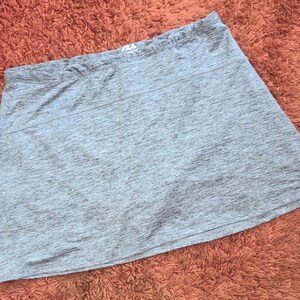 May include: A gray athletic skirt with a slightly flared design. The skirt has a comfortable waistband and a subtle textured pattern. The Fila logo is visible on the waistband. This activewear skirt is suitable for various sports and activities.