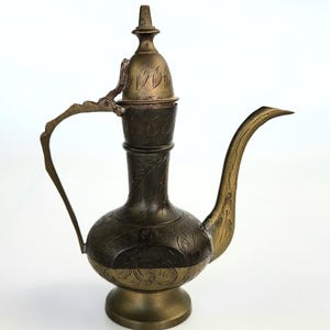 Puede incluir: Una pequeña tetera de latón adornada con una tapa y un pico curvo. La tetera está decorada con intrincados patrones florales.