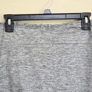 May include: A gray heathered skirt hangs from a black hanger. The skirt has a wide waistband and a subtle texture. The fabric appears to be a soft, comfortable material, suitable for casual wear. The skirt is a neutral color, making it versatile.