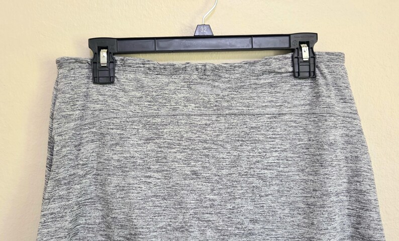May include: A gray heathered skirt hangs from a black hanger. The skirt has a wide waistband and a subtle texture. The fabric appears to be a soft, comfortable material, suitable for casual wear. The skirt is a neutral color, making it versatile.