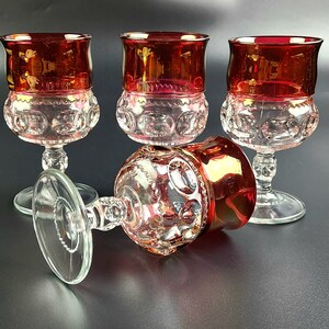 May include: Four clear glass goblets with a red, ruby-like colored base. The goblets have a textured, raised pattern of small circles.