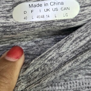 May include: Close-up of a gray and white athletic top with the Fila logo. The tag reads "Made in China" with size information. The fabric has a textured, heathered appearance.
