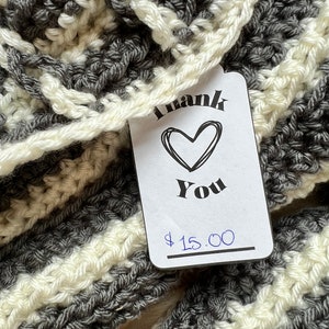May include: A gray and white striped crocheted scarf with a price tag that says "Thank You" and "$15.00".