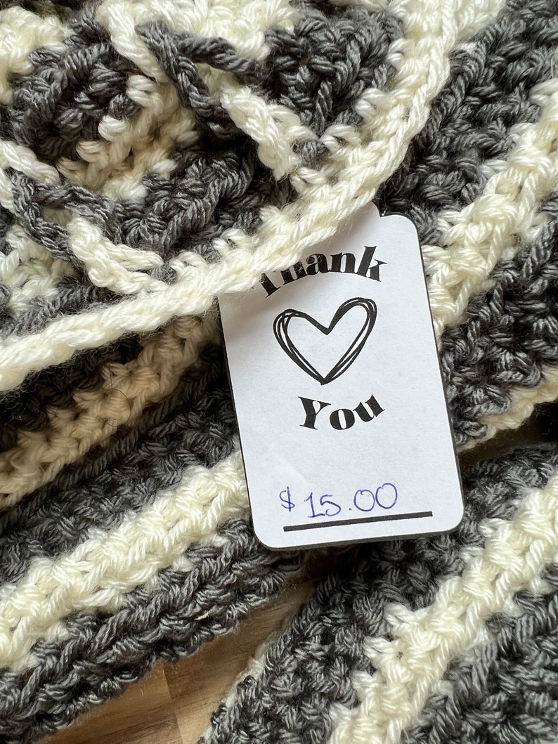May include: A gray and white striped crocheted scarf with a price tag that says "Thank You" and "$15.00".