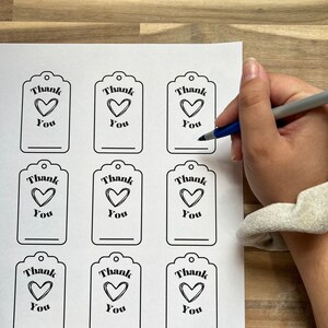 May include: Printable sheet of nine gift tags with a black outline. Each tag has a heart with the text "Thank You" above it.