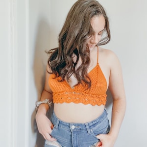 May include: A woman wearing a burnt orange crochet top and denim shorts.