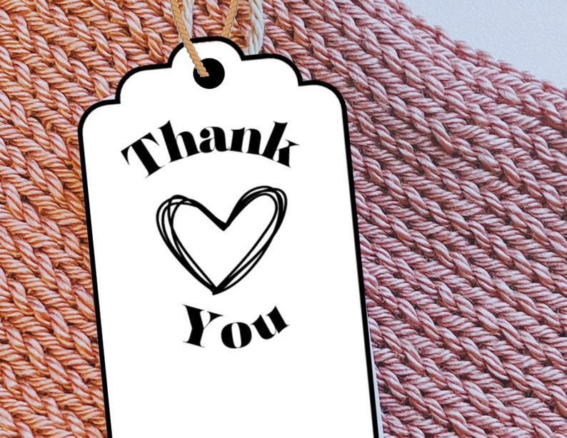 May include: A white gift tag with black text that says "Thank You" with a heart drawn in the middle. The tag is on a pink and orange woven background.
