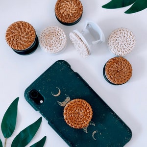 May include: A green phone case with a moon and stars design and a brown woven phone grip.