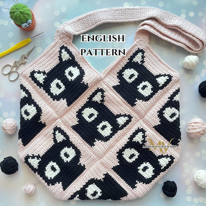 May include: A crochet tote bag with a pink background and black cat faces. The bag has a long strap and is made with a simple stitch pattern. The text "ENGLISH PATTERN" is written in black on the bag.