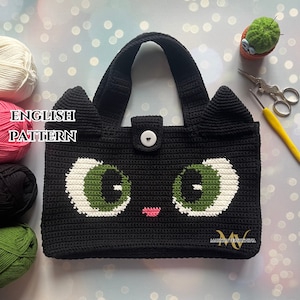 Może przedstawiać: Czarna torba na zakupy zrobiona na szydełku z wzorem twarzy kota. Torba ma białe oczy z zielonymi źrenicami, różowy nos i dwa czarne uszy. Torba ma zapięcie na guzik i dwa uchwyty.