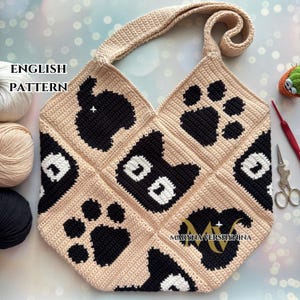 Könnte beinhalten: Eine gehäkelte Tragetasche mit einem schwarz-weißen Pfotenabdruck- und Katzenkopfdesign. Die Tasche ist beige und hat einen langen Riemen. Der Text "ENGLISH PATTERN" ist in der oberen linken Ecke des Bildes sichtbar.