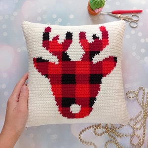 May include: A white crocheted pillow with a red and black buffalo plaid reindeer design.
