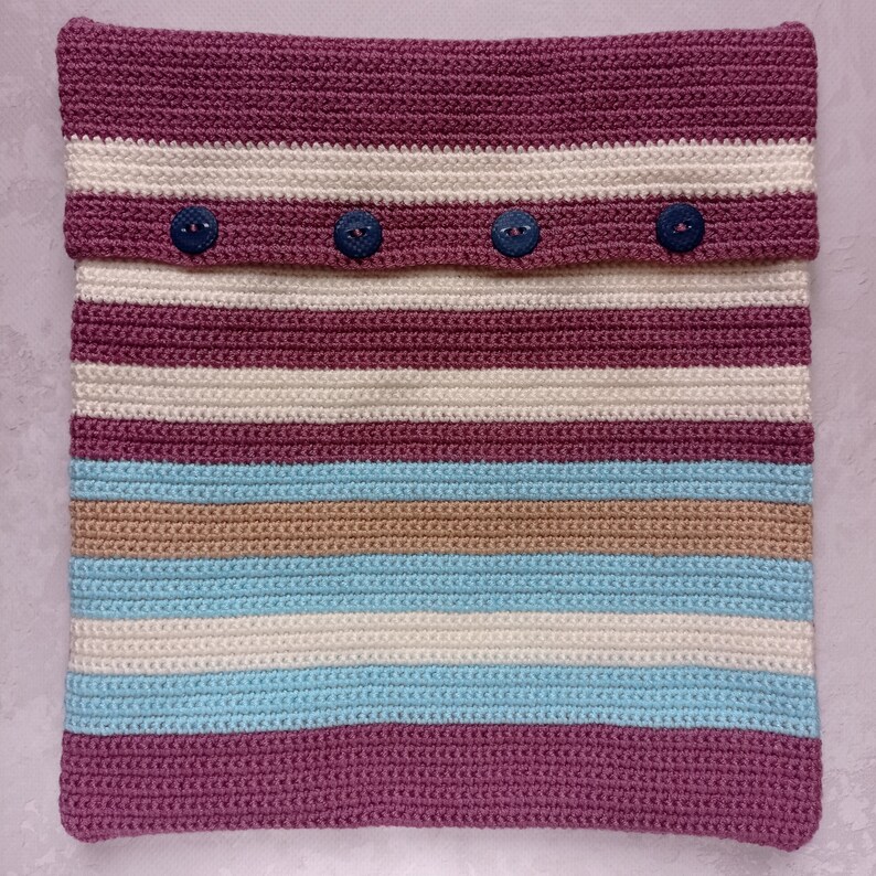 May include: A striped crocheted pillow with a burgundy, beige, white, and light blue color scheme. The pillow has four buttons on the top flap.