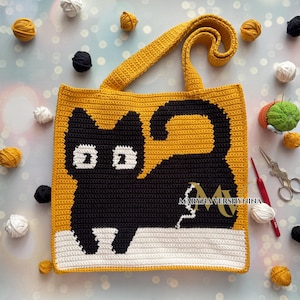 May include: A handmade, crochet tote bag featuring a black cat design on a mustard yellow background. The cat is lying down on a white surface. The bag has a matching yellow strap. The background includes yarn balls and crafting tools.