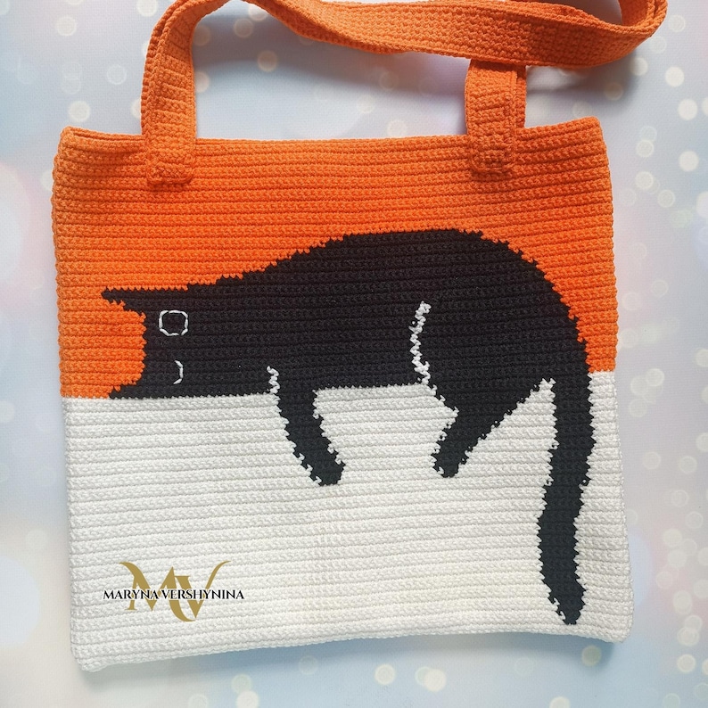 May include: A crocheted tote bag with orange and white stripes. A black cat is crocheted onto the bag. The bag has a black handle and the text "MARYNA VERSHYNINA" is printed on the bottom.
