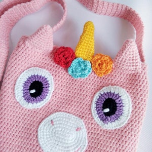 May include: A pink crocheted unicorn bag with a yellow horn, rainbow colored flowers, and purple and white eyes. The bag has a pink crocheted strap.