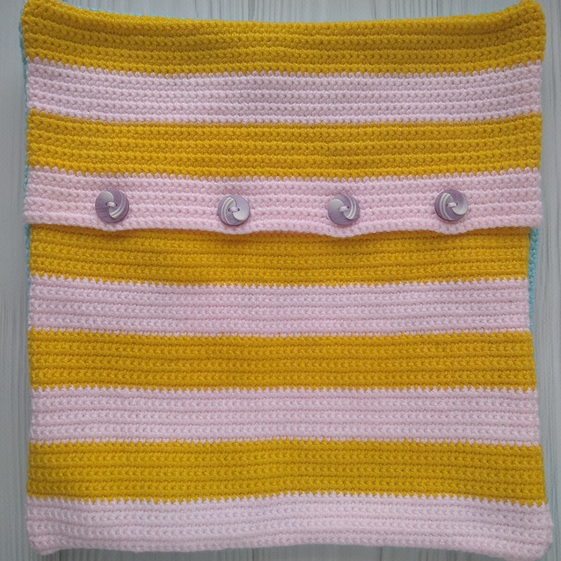 May include: A yellow and pink striped crocheted pillow cover with four buttons.