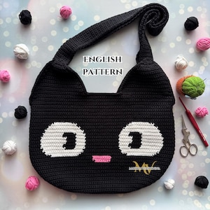 Op de afbeelding: Zwarte gebreide tas in de vorm van een kat met witte ogen en een roze neus. De tas heeft een lange schouderband en de tekst "ENGLISH PATTERN" staat in wit op een zwarte achtergrond.