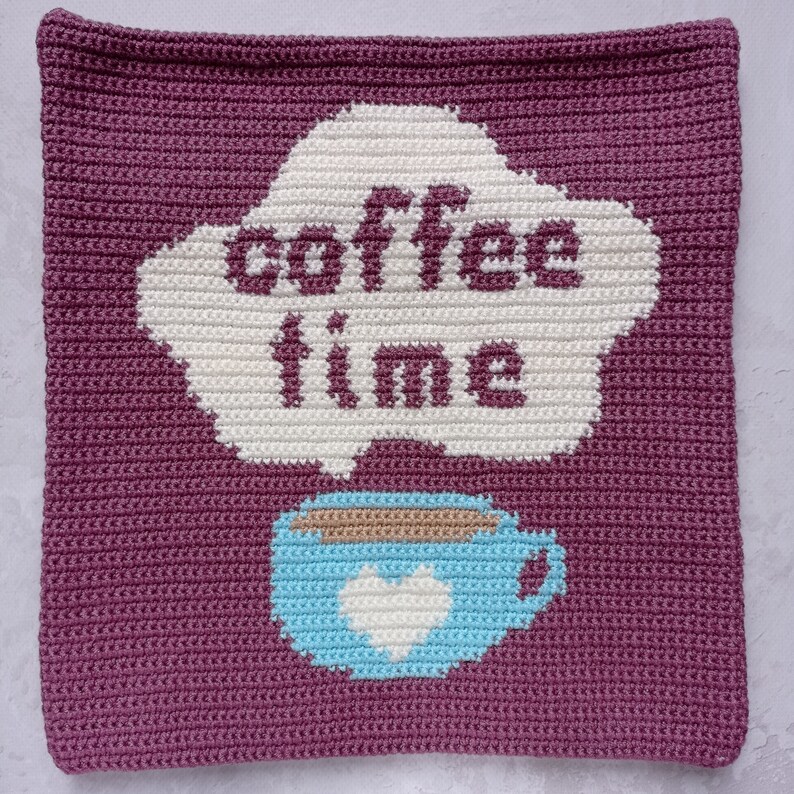 May include: A crocheted square pillow with a purple background and a white cloud with the text "coffee time" and a blue coffee cup with a white heart.