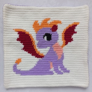 May include: A crocheted pillow with a purple dragon design. The dragon has orange flames, red wings, and a pink belly.