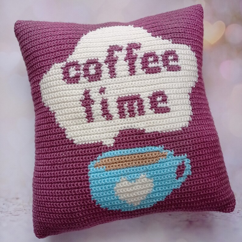 May include: A purple crocheted pillow with a white cloud shape that says "coffee time" and a blue coffee cup with a white heart.