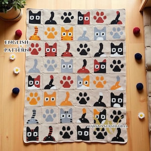 Puede incluir: Una manta de ganchillo beige con un patrón repetido de caras de gato, patas y colas en negro, naranja, rojo y gris. La manta tiene el texto "ENGLISH PATTERN" y "MARYNA VERSHYNINA".
