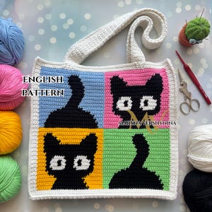 May include: Crochet tote bag featuring a black cat design in four different coloured squares: blue, pink, green, and yellow. The bag has a white strap and is made with a textured stitch.