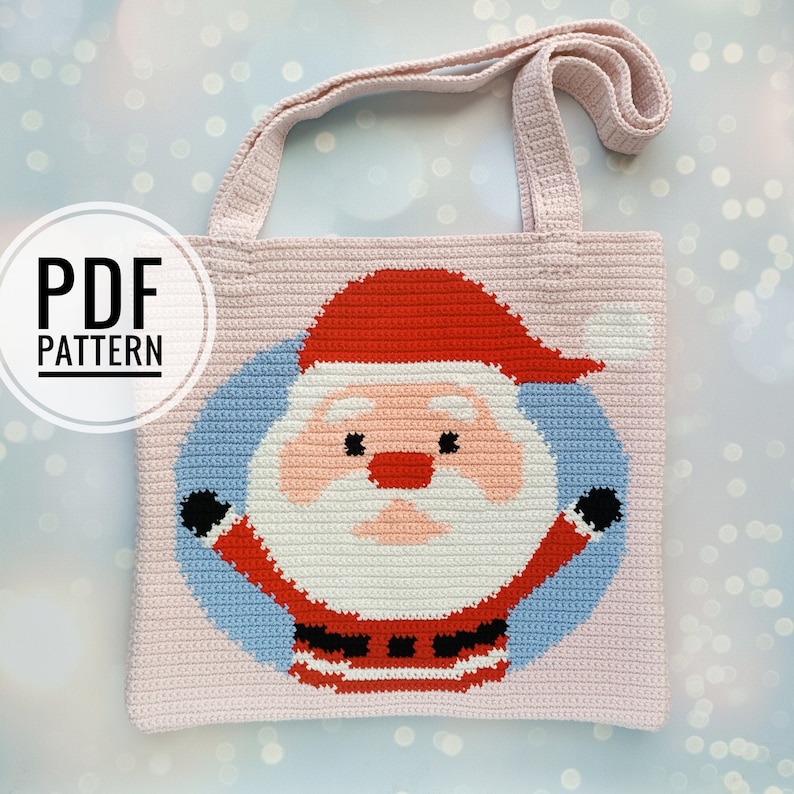 May include: A light pink crocheted tote bag with a Santa Claus design. The Santa Claus image is in the centre, with a red hat, white beard, and a blue background. The bag has a matching pink handle and the text "PDF PATTERN".