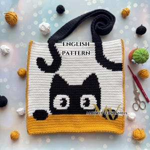 Op de afbeelding: Een handgemaakte gehaakte tote bag met een zwart kattenontwerp op een wit en grijs gestreepte achtergrond. De tas heeft een zwart handvat en een gele rand. De tekst "ENGLISH PATTERN" is zichtbaar op de tas.