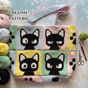 Op de afbeelding: Een gehaakte draagtas met een zwart kattenontwerp op een patchwork van pastelkleurige vierkanten. De tas heeft een lichtblauw handvat. De tekst "ENGLISH PATTERN" is zichtbaar. Verschillende gekleurde garenbollen zijn zichtbaar.