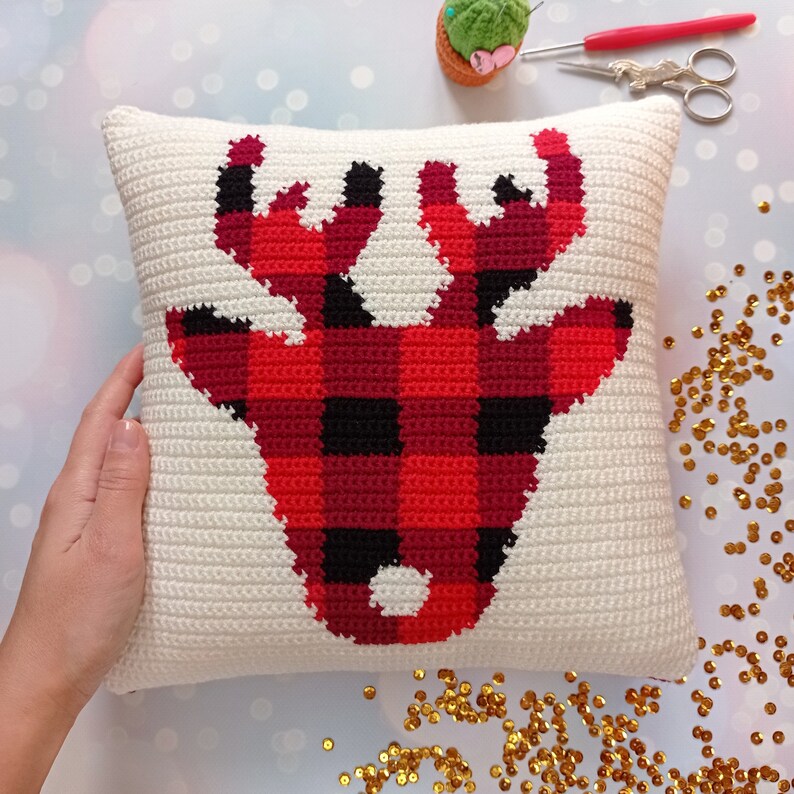 May include: A white crocheted pillow with a red and black buffalo plaid reindeer design.